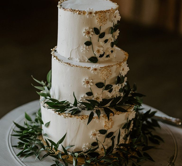 White three tier rustic wedding cake with iced flowers and green foliage 