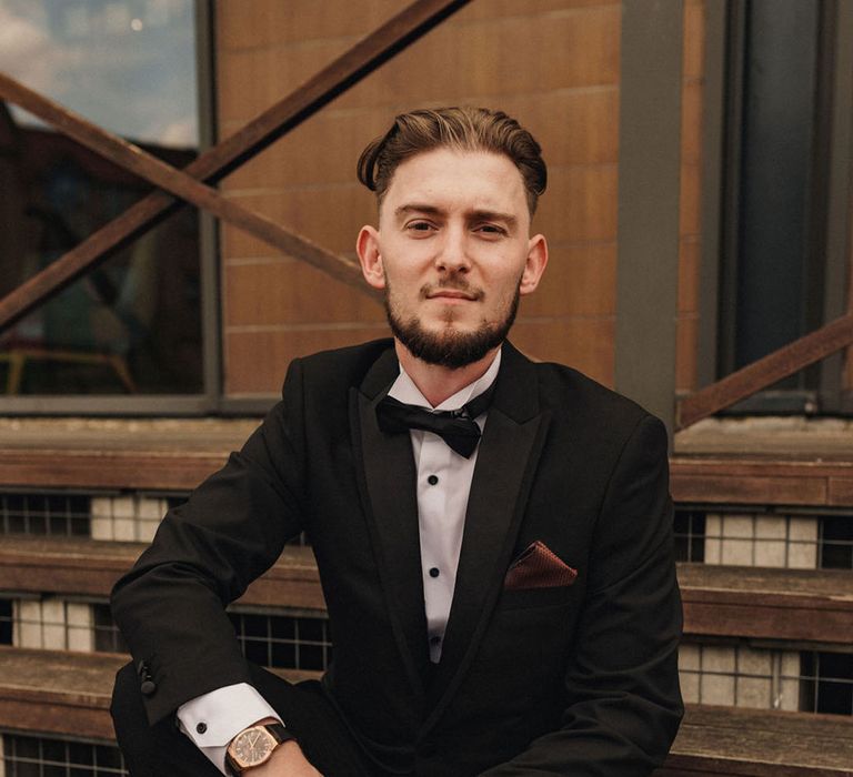 Groom in black tuxedo sits for traditional and classic wedding 