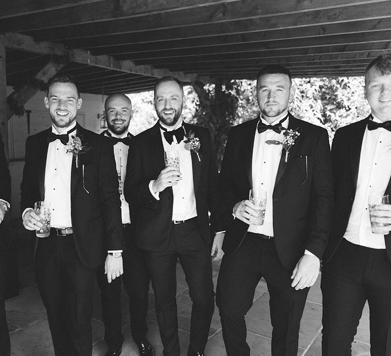 Groomsmen wearing black tie wedding tuxedos with floral buttonhole accessories 