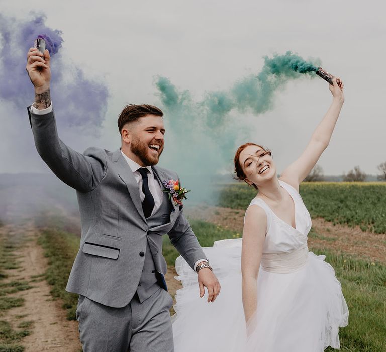 The bride and groom waving green and purple smoke bombs for the wedding photographs 