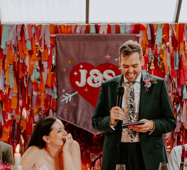 Groom in dark green suit reading out his wedding speech at the industrial style wedding 