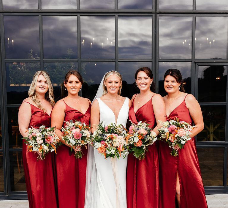 Bridal party wearing red satin bridesmaid dresses with the bride in a plunging wedding dress 