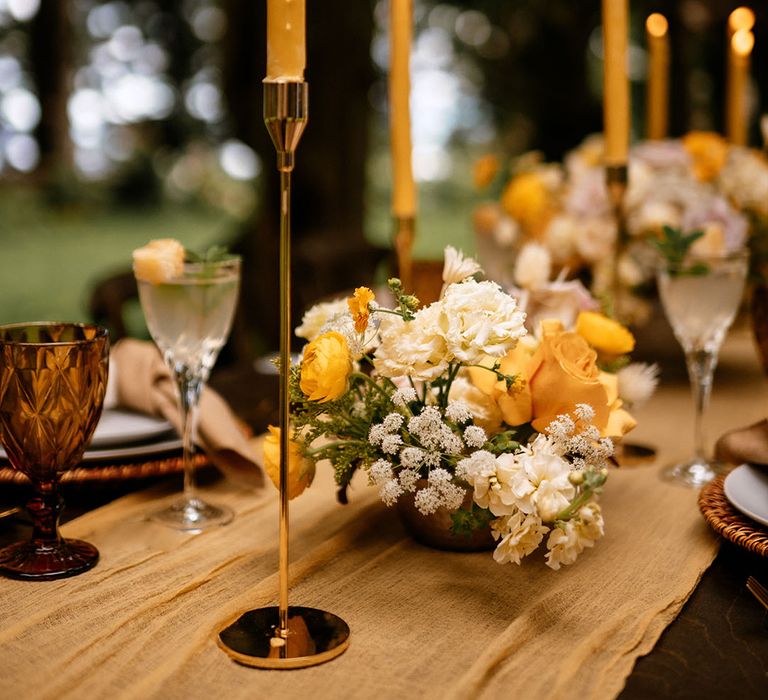 Yellow roses and white flowers in table centrepiece arrangements with gold candleholders and yellow candles 