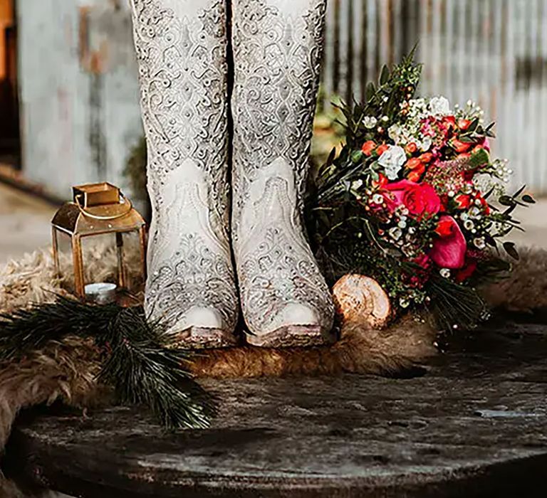 Image of white bridal cowboy boots next to a bouquet of flowers by Sonder Lust Photography