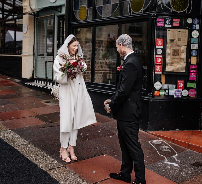 Bride and groom first look with bride in ivory jumpsuit and coat 