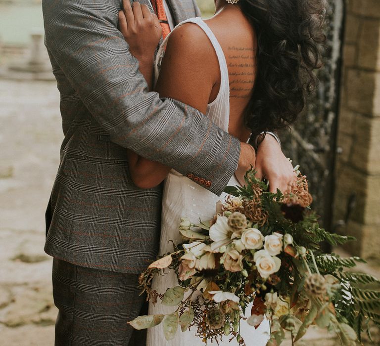 Groom in grey check suit embracing his bride in a low back dress