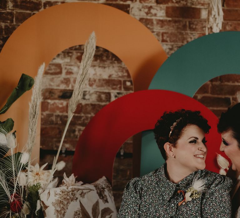 Two brides sitting at a 70s altar with dried flowers 