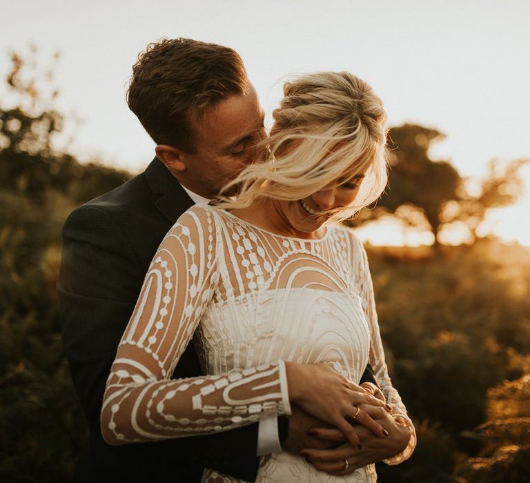 Groom embracing his bride in a long sleeve wedding dress