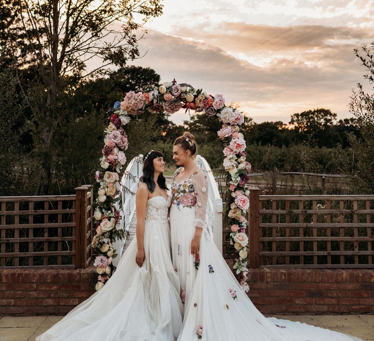 Bride in romantic wedding dresses standing next to a floral arch 