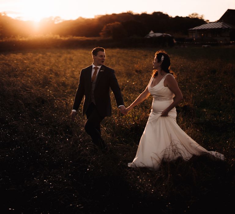 Bride & groom walk through the countryside during golden hour