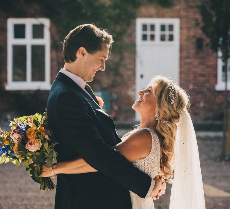 Smiling bride in Justin Alexander wedding dress holding colourful bouquet hugs groom in the grounds at Iscoyd Park