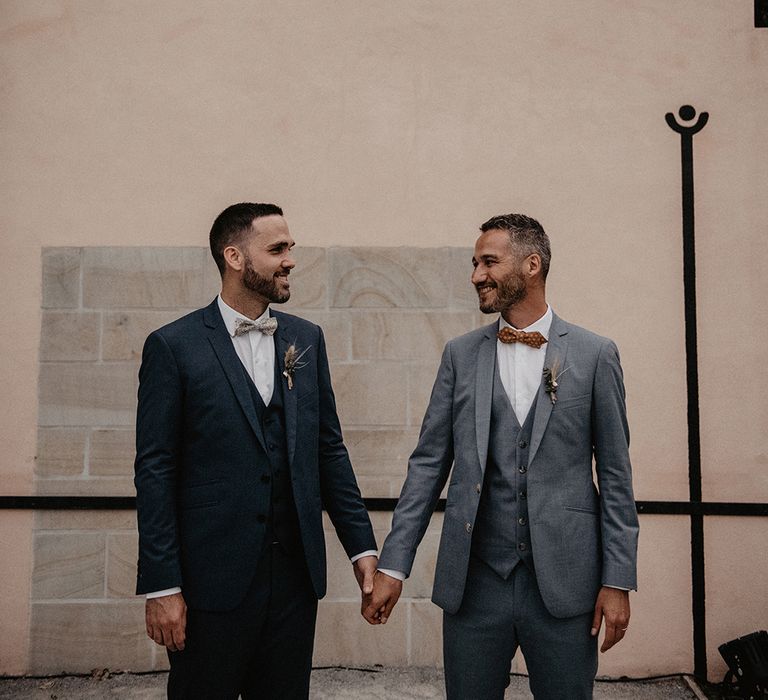 Two grooms in blue three-piece suits with brown bow ties and dried flower buttonholes | Patricia Hendrychova-Estanguet Photography