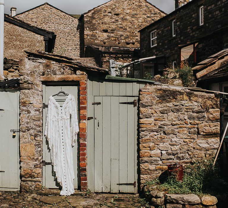 Lace wedding gown with bell sleeves hangs in front of wooden door outside