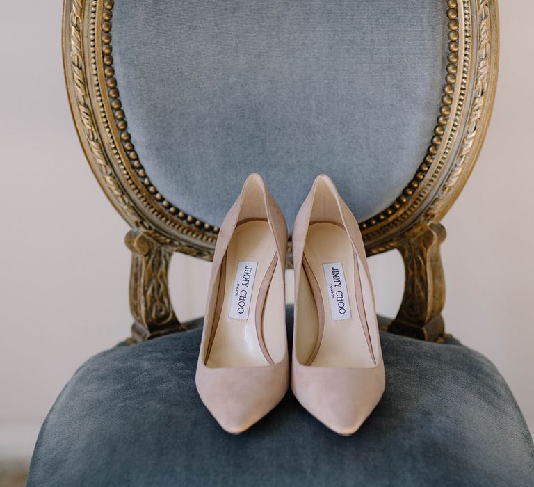 Blush pink Jimmy Choo shoes on a blue velvet seat