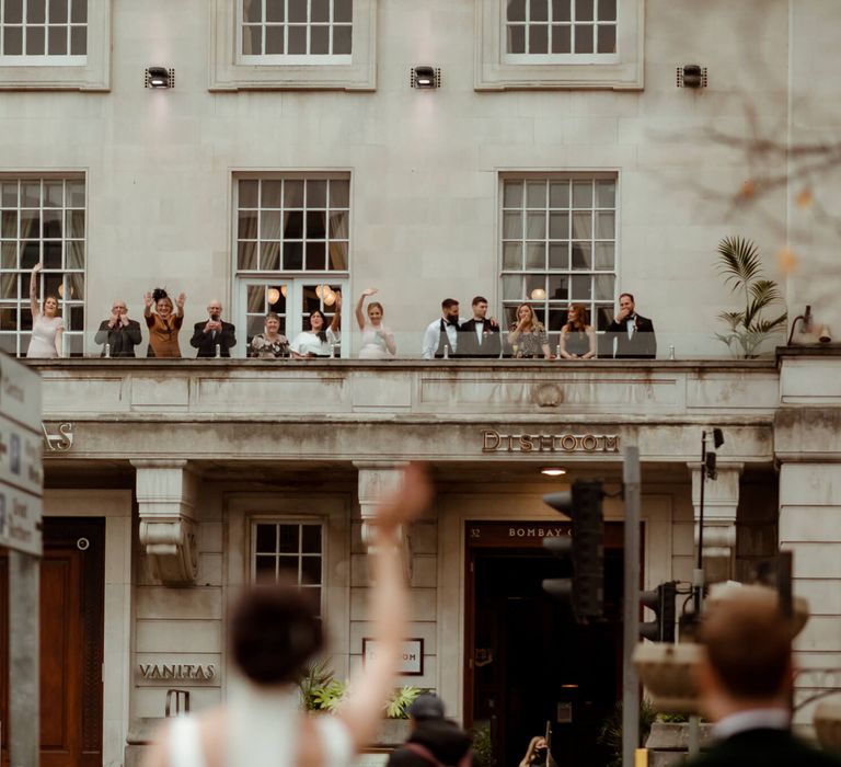 Wedding guests waving at bride and groom from the outdoor patio as they arrive at their wedding venue