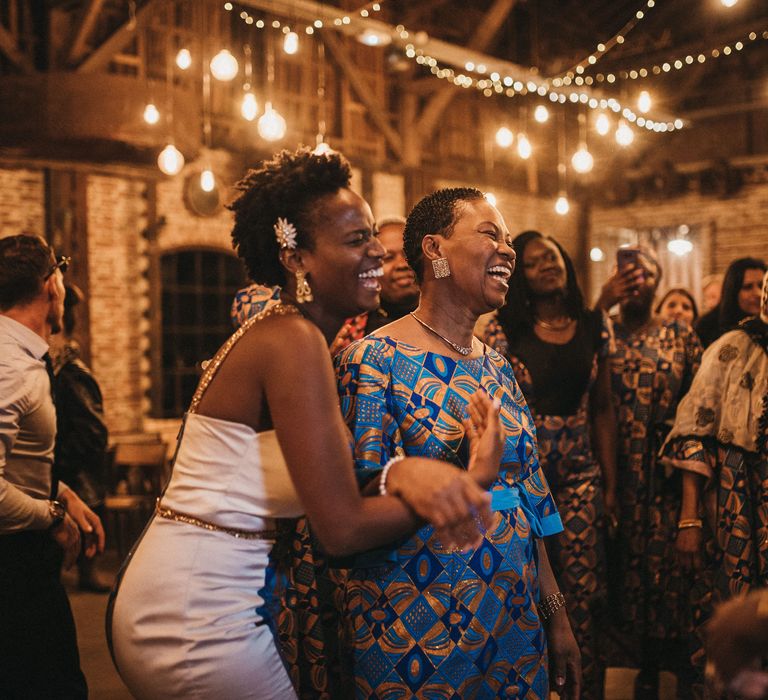 West African bride and wedding guest dancing at the festoon lit reception 