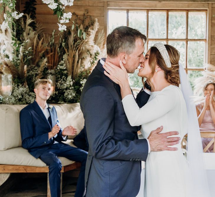 Bride in Elbeth Gillis gown and beaded bridal headband kisses groom in navy Cad & the Dandy suit at Eurdige Manor wedding