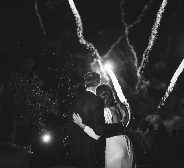 Bride in Elbeth Gillis gown stands arm in arm with groom watching fireworks at Euridge Manor wedding