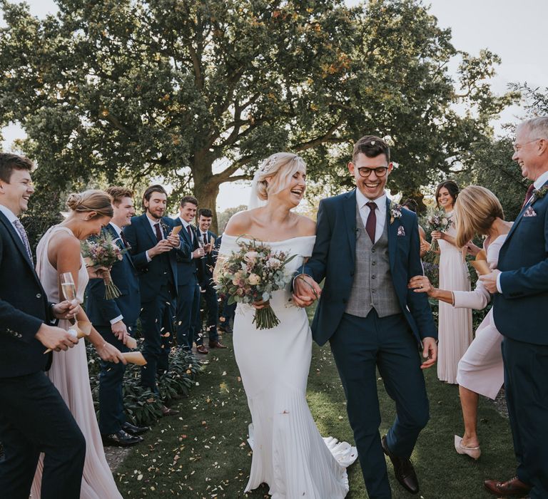 Bride & groom hold hands as they walk through wedding party throwing confetti 