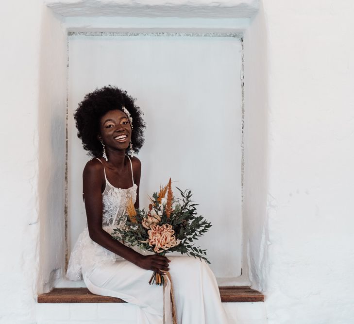 Beautiful bride in a fitted wedding dress with lace peplum bodice sitting in an alcove at Ponden Mill 