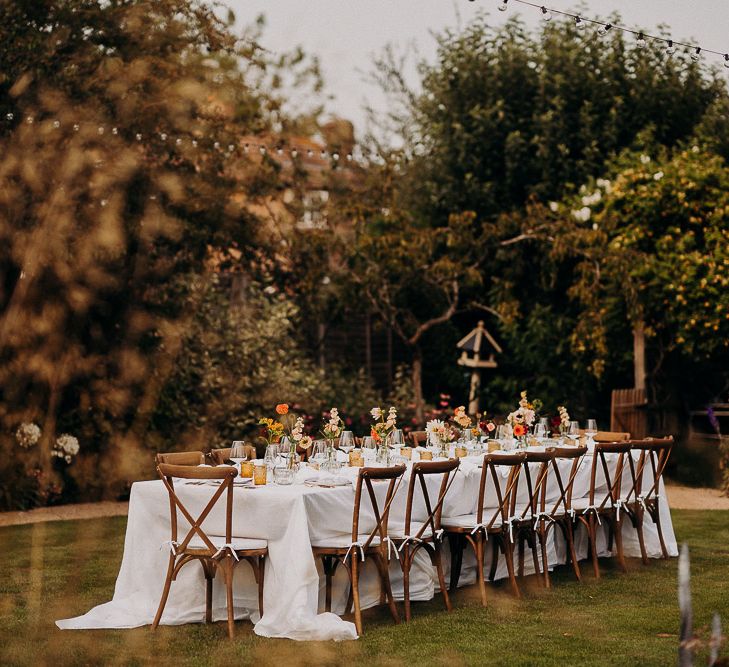 Garden party wedding reception with wooden table and chairs and coloured glass goblets 