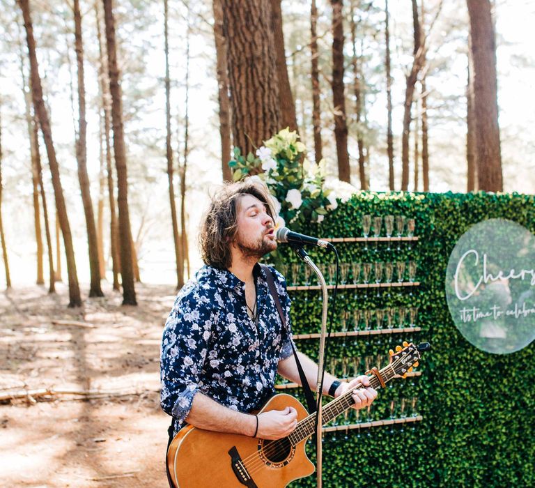 Acoustic singer stands in front of Prosecco wall