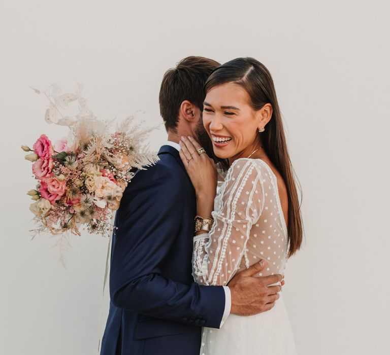 Bride in a polka dot Marylise Bridal gown with long sleeves embracing her husband in a navy suit 