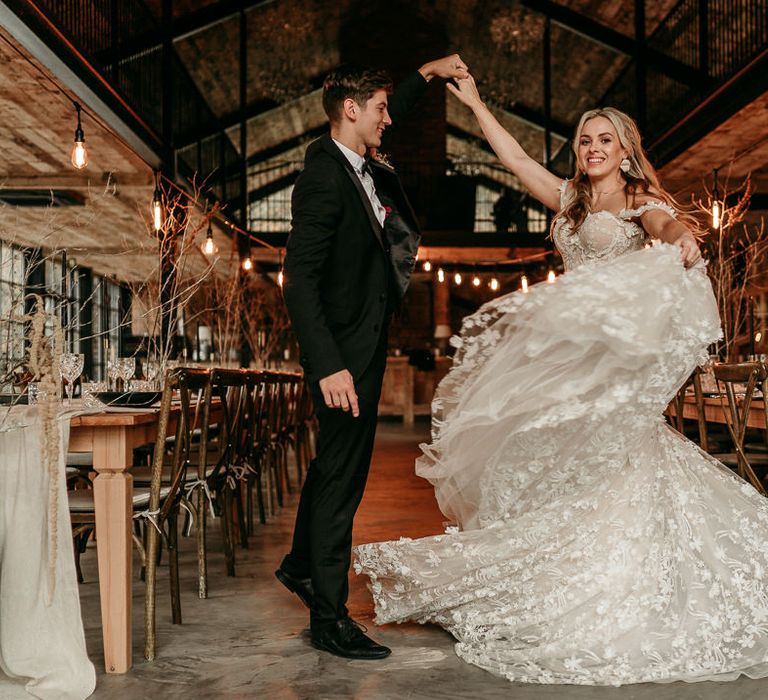 Groom in a black tuxedo twilling his bride in a appliqué wedding dress at The Hidden River Cabins wedding venue