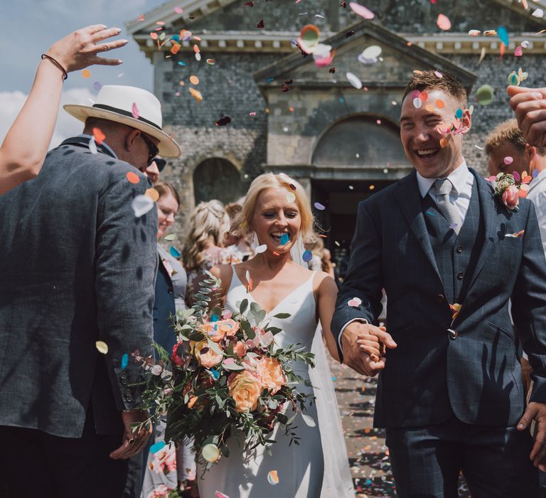 Couple leave church whilst colourful confetti blows around them 