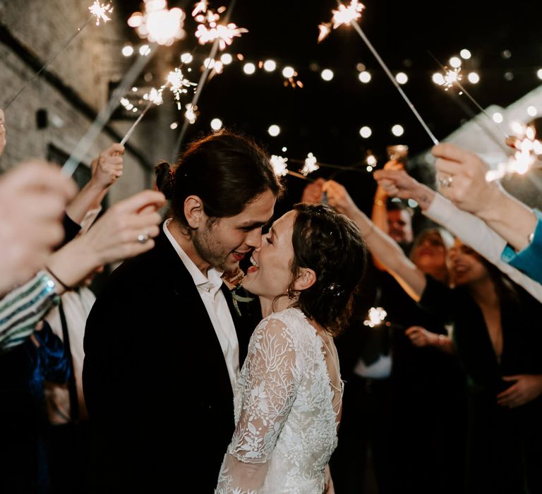 Bride and groom walking under guests arms as they hold sparklers as an archway