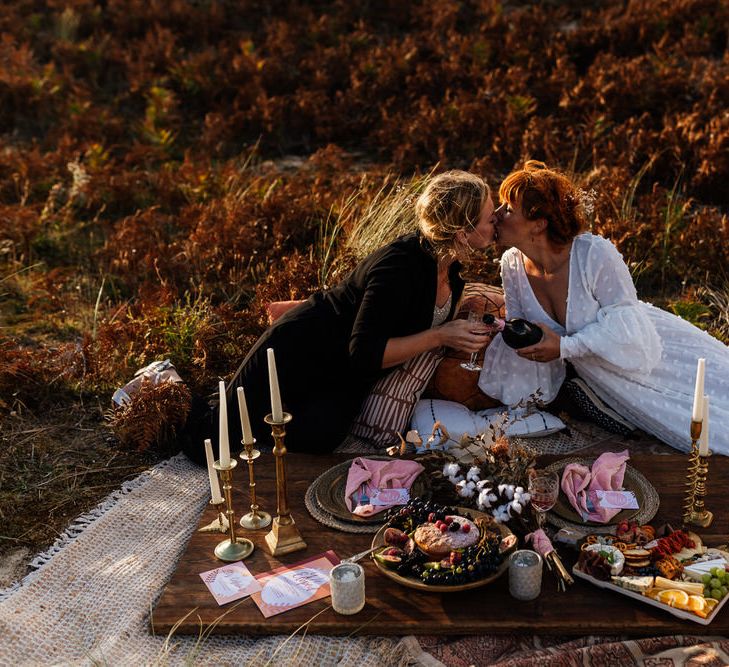 Same-sex couple kissing at sunset over beach picnic