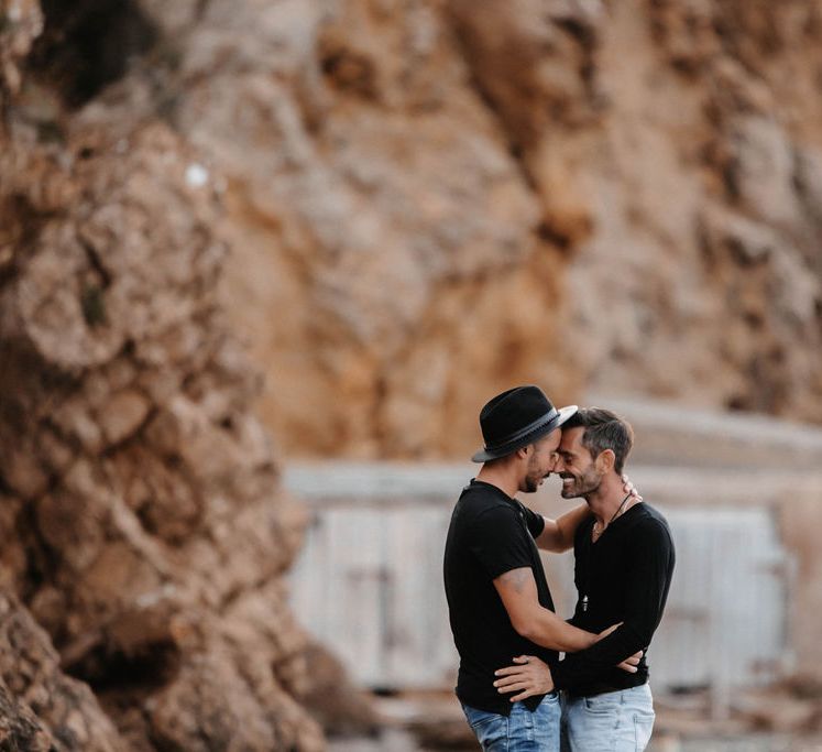 Grooms stand in front of rocks and kiss whilst wearing black T-shirts and pale blue jeans