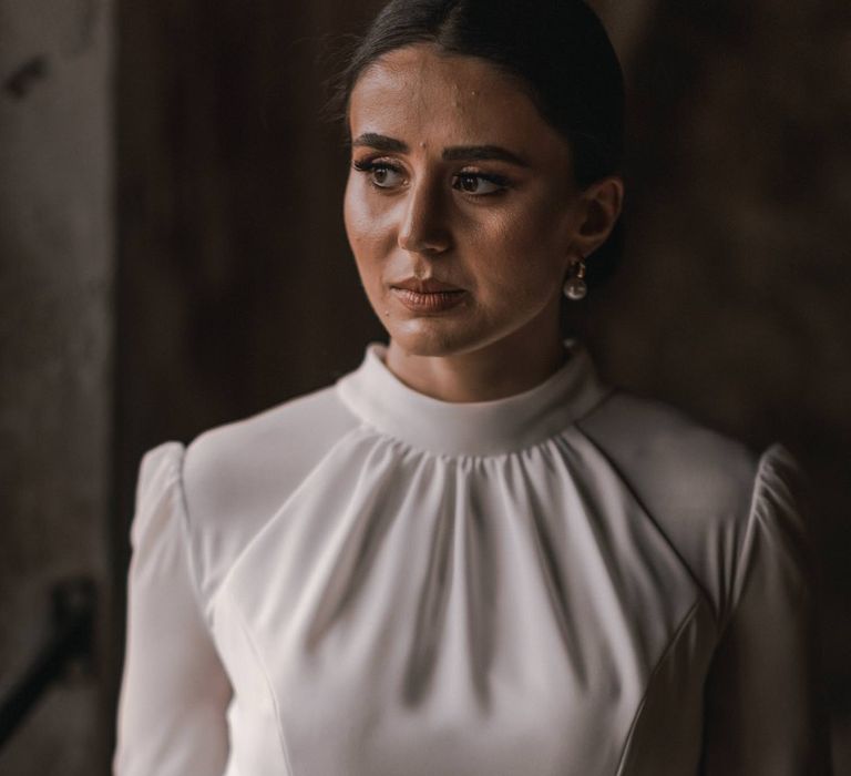 Bride wears high neck wedding gown and has her black hair tied back