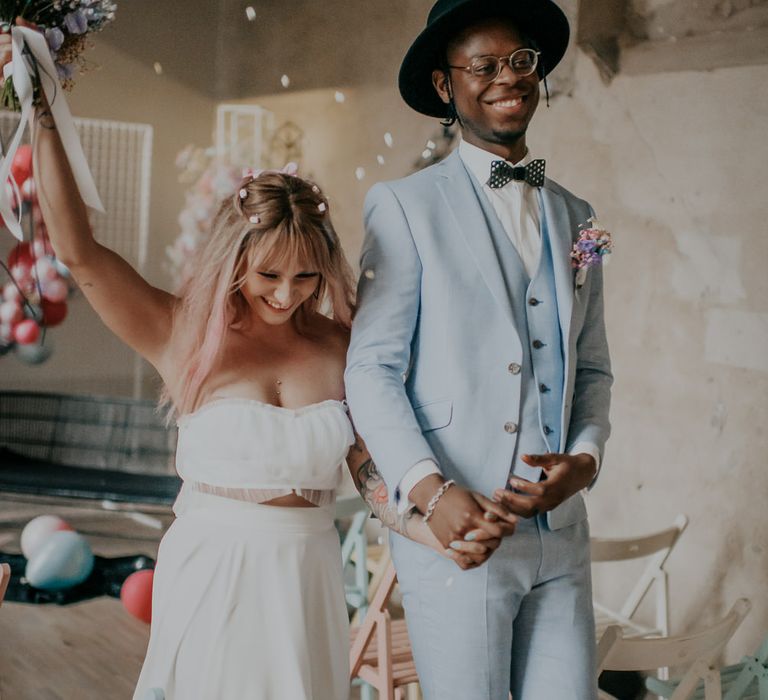 Happy bride in separates and groom in coloured suit descending up the aisle as husband and wife 