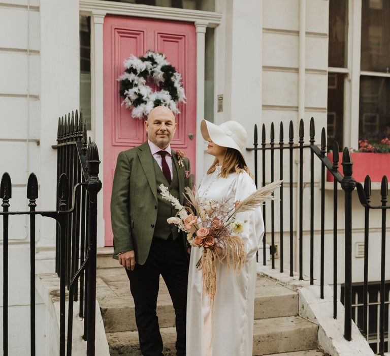 Bride & groom stand in front of pink door in Chelsea