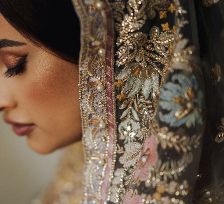 Indian bride with brown eyeshadow and eyeliner, blush cheeks and deep red lipstick wearing a beaded wedding veil