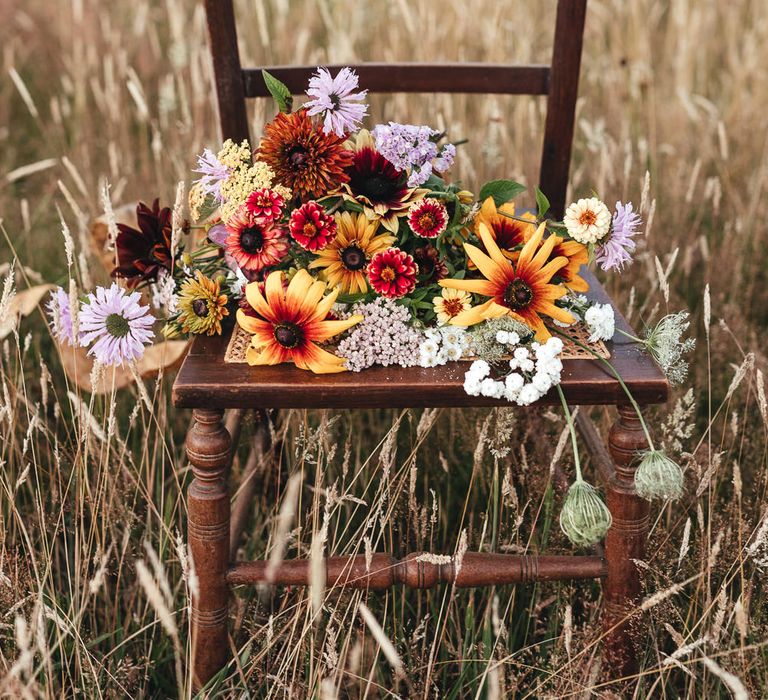 Bright floral bouquet sits on wooden chair for boho chic outdoor wedding ceremony