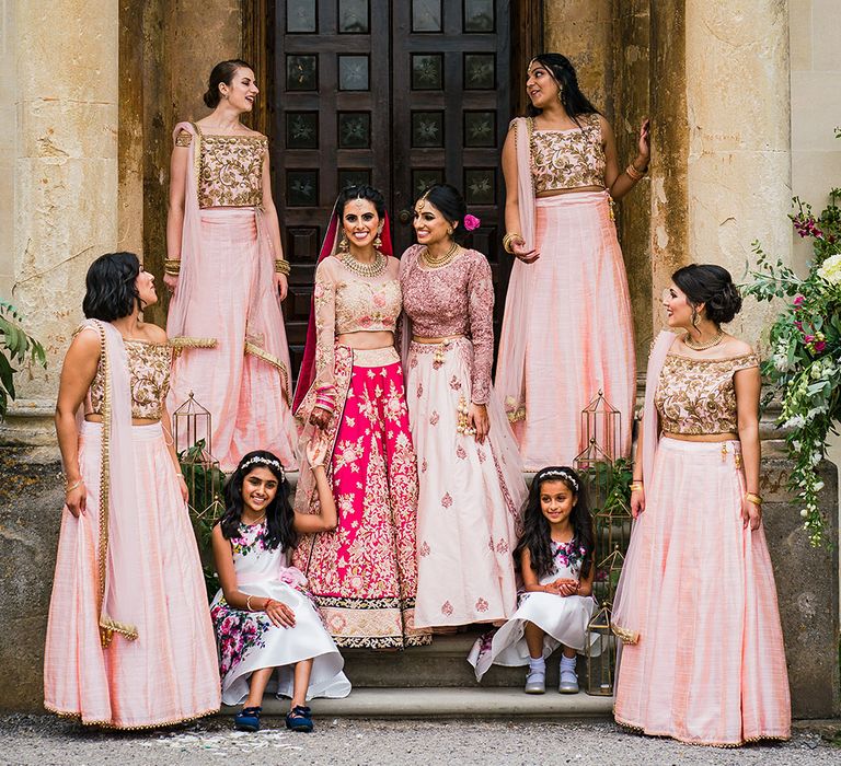 An Indian bride stands with all of her bridesmaids. They all wear pink and are laughing.