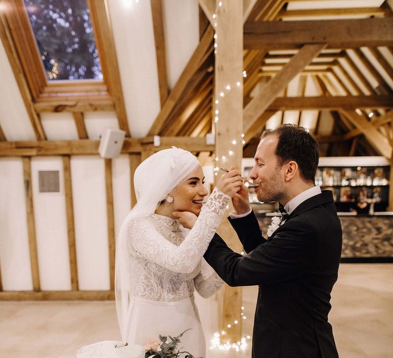 Bride feeds groom slice from two-tier pale green wedding cake on tree trunk stand 