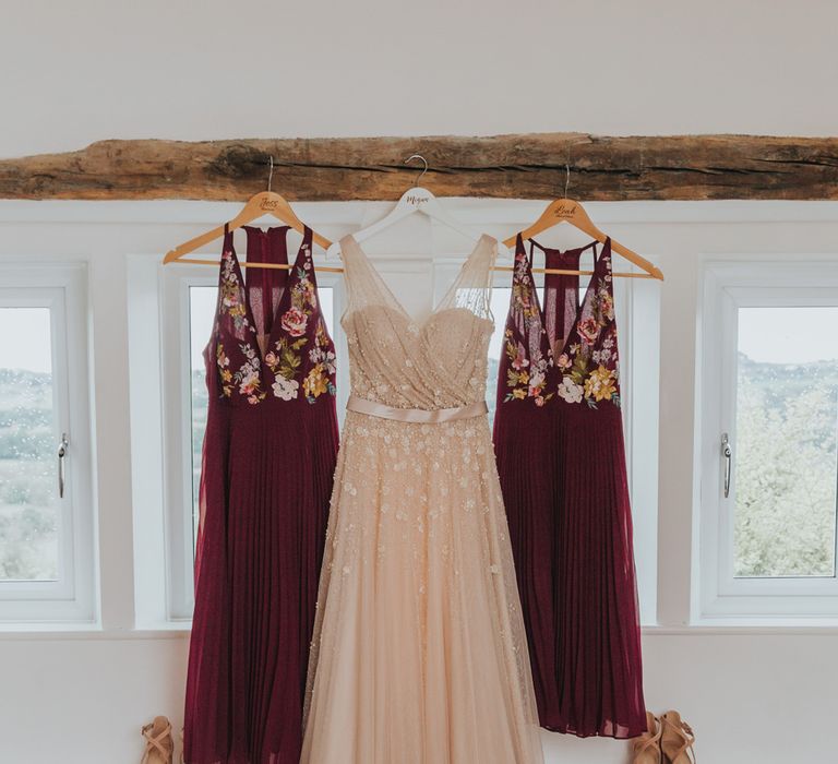 Pearl wedding dress hangs next to burgundy embroidered bridesmaids dresses before barn wedding ceremony - Maddie Farris Photography