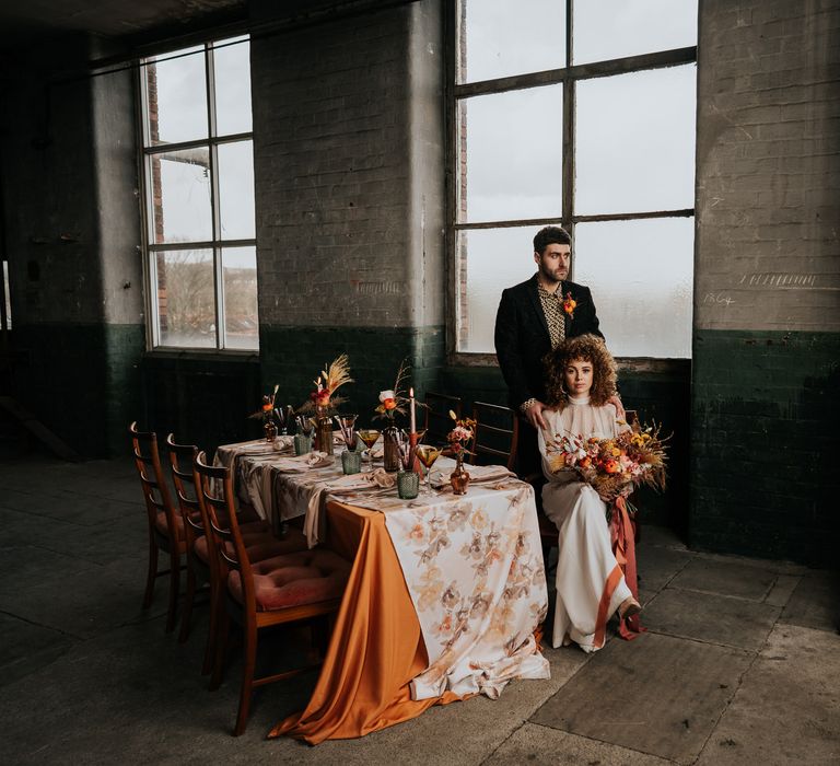 Bride and groom sitting at an intimate tablescape in an industrial venue with patterned tablecloth and coloured glassware