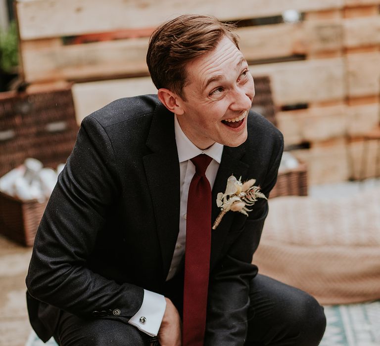 Groom in a black suit and burgundy tie 