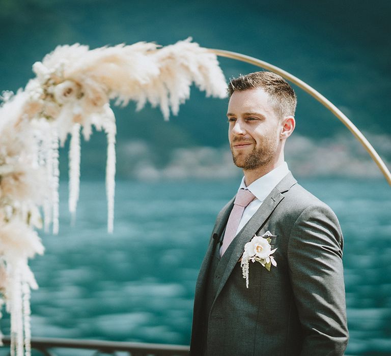 Groom waits for his bride in front of floral installation