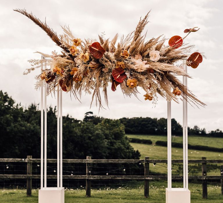 White rectangular arch with burnt orange, yellow and ivory pampas grass cloud for summer wedding in Dorset