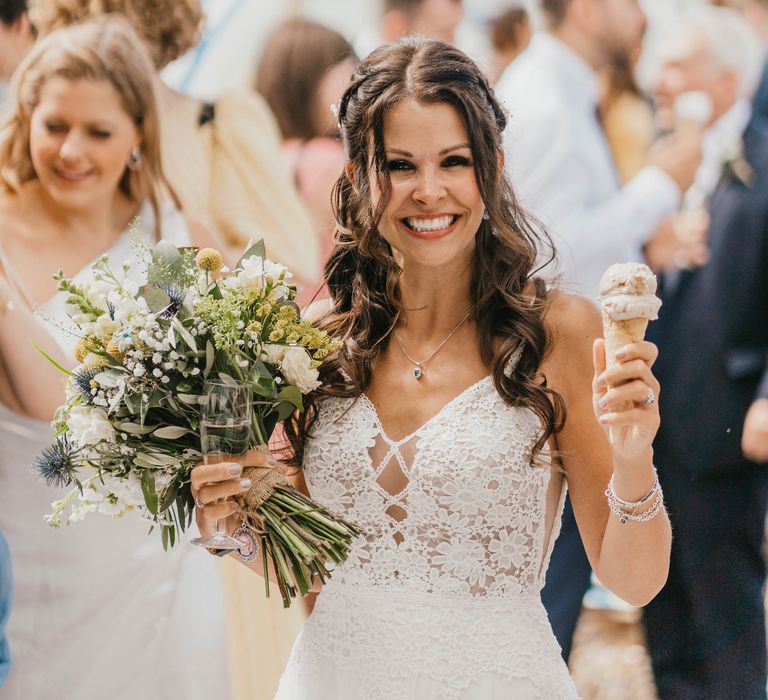 Bride smiles and holds her floral bouquet as she wears her brown hair in loose curls 