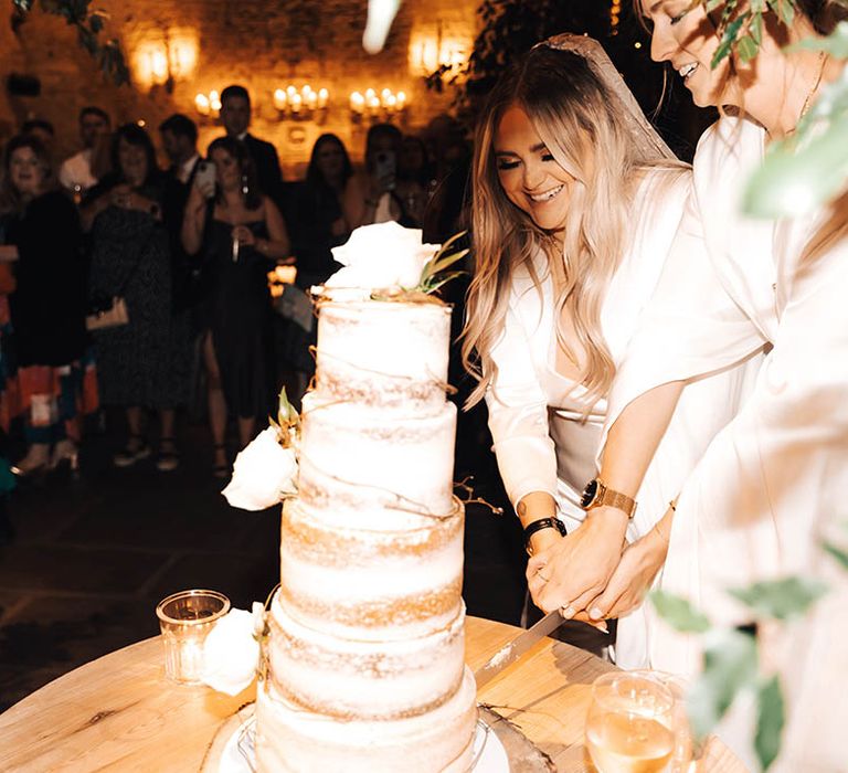 Brides cut naked cake as wedding guests watch on