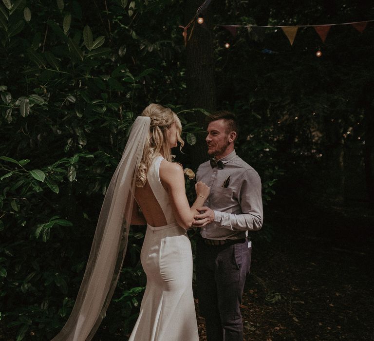 Bride & groom hold one another as bride wears floor-length veil and backless dress