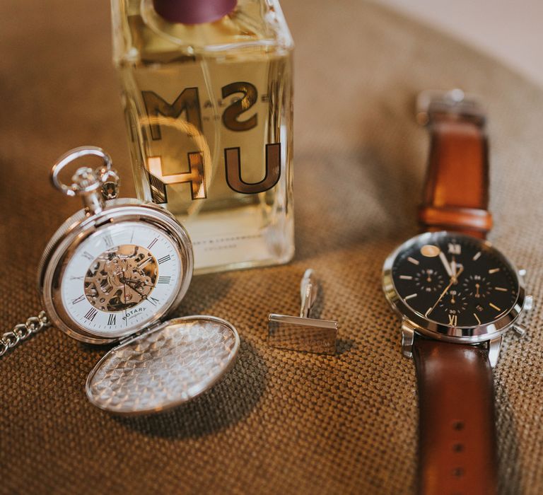 Groom's Jo Malone cologne, pocket watch, cufflink and watch laid out before Tythe Barn wedding with barn wedding flowers