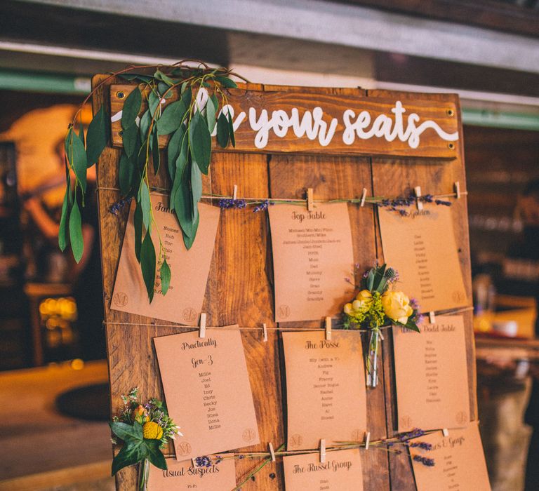 Rustic table plan on wooden board with brown paper stationery and hung up with string and mini pegs surrounded by foliage | Story + Colour