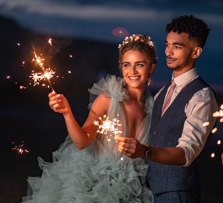 Sparkler moment on the beach with bride in a coloured frilly wedding dress and groom a wool waistcoat 